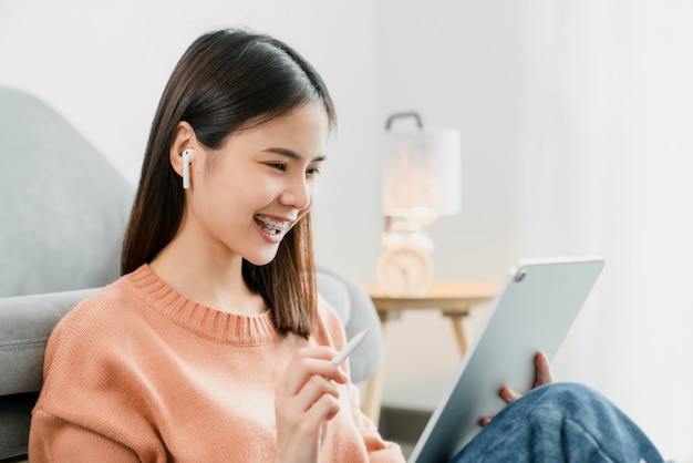 Young Asian woman using digital tablet and listen music to relaxing on the sofa at the house.