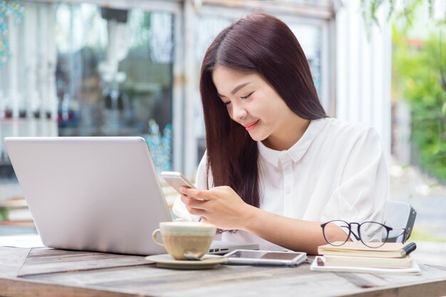 Giovane donna asiatica usando il suo computer portatile e smart phone