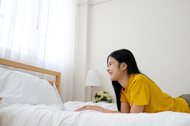 Young asian woman using laptop computer sitting in front of white brick wall background 