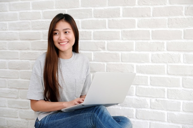 Young asian woman using laptop computer sitting in front of white wall background with cop