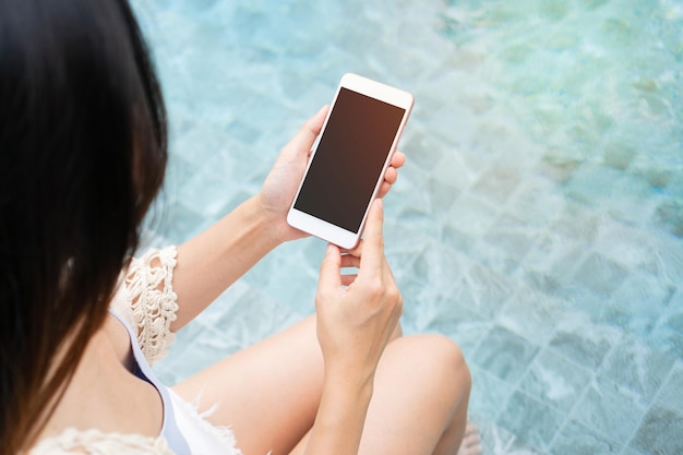 휴대 전화를 사용하고 수영장 옆에 앉아있는 젊은 아시아 여성 여름 휴가 기술 및 라이프 스타일 개념 복사 공간 상위 뷰