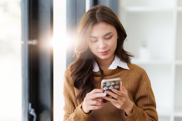 Young Asian Woman using smart phone at home Female holding cellphone checking email or social media on internet