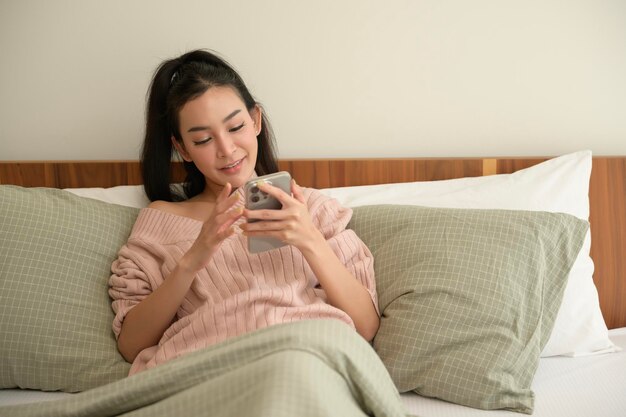 Young asian woman using smart phone lying on bed