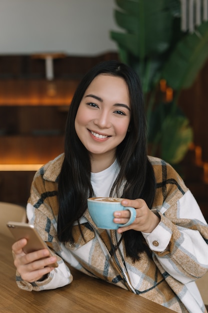 Young Asian woman using smartphone, drinking coffee in cafe