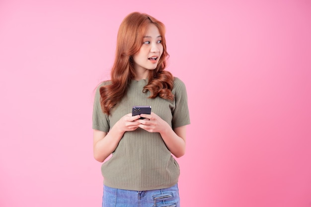 ピンクの背景にスマートフォンを使用して若いアジアの女性