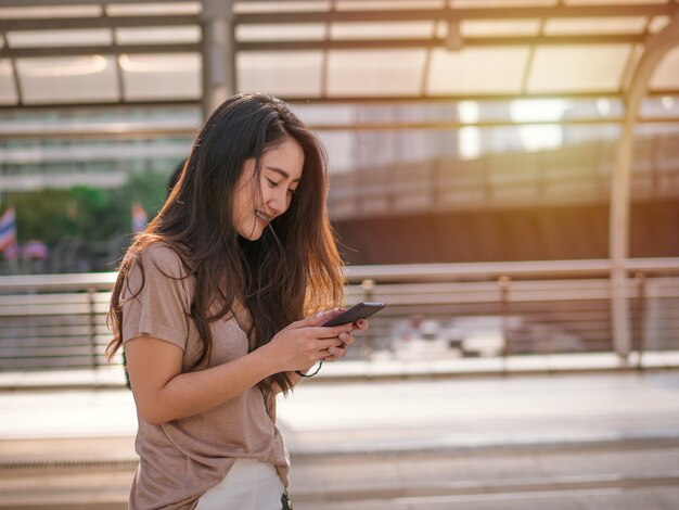 都市のソーシャルメディアを探しているスマートフォンを使用している若いアジア人女性。