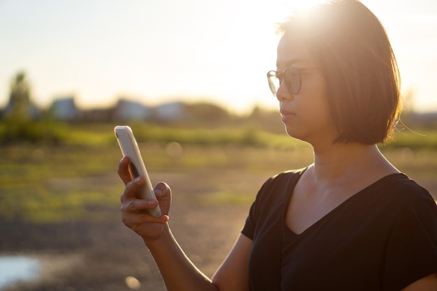 日没時にスマートフォンを使用して若いアジアの女性。