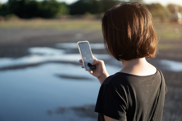 日没時にスマートフォンを使用して若いアジアの女性。