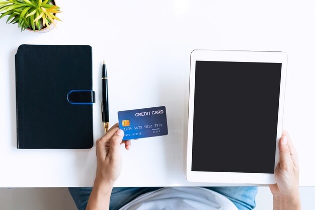 Young Asian woman using tablet while holding credit card on desk in the living room at home, top view and copy space.