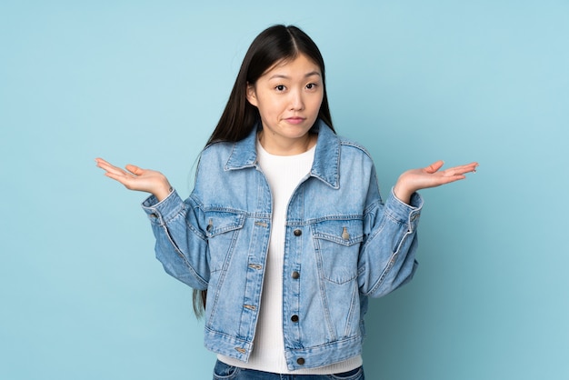 Young asian woman on wall having doubts while raising hands