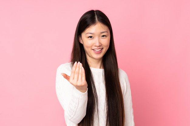 Young asian woman over wall inviting to come with hand