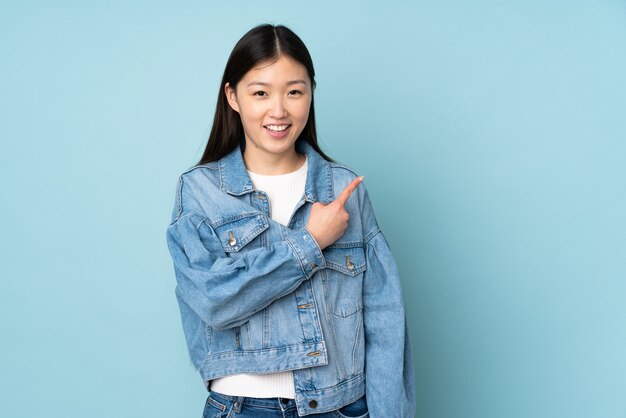 Young asian woman on wall pointing to the side