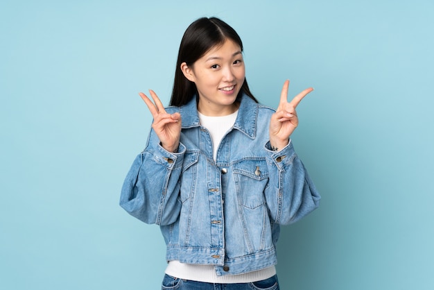 Young asian woman on wall showing victory sign with both hands