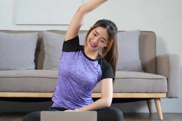 Young asian woman watching fitness video on laptop and stretching arm to relaxing after exercise