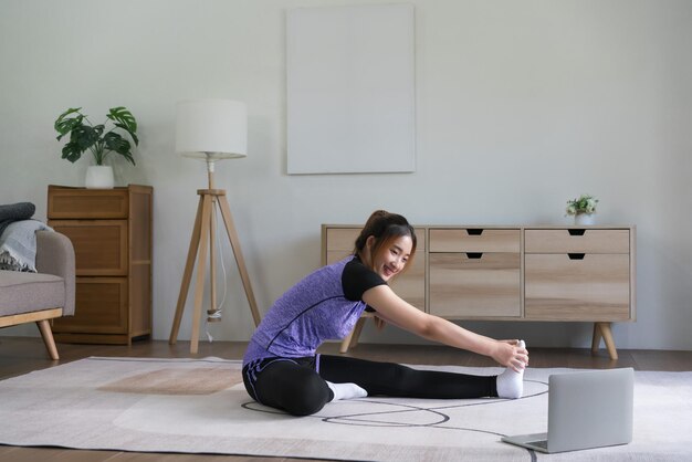 Young asian woman watching fitness video on laptop to training and doing exercise to stretching leg