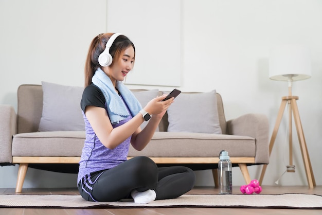 アジアの若い女性はヘッドフォンを着けてインターネットをサーフィンし、運動後にスマートフォンで音楽を聴く