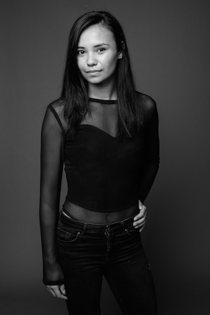 young Asian woman wearing black long sleeved shirt against gray wall. black and white