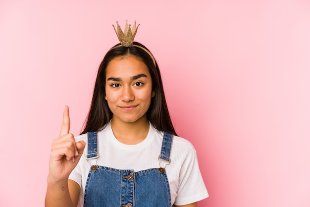 Young asian woman wearing a crown isolated showing number one with finger.