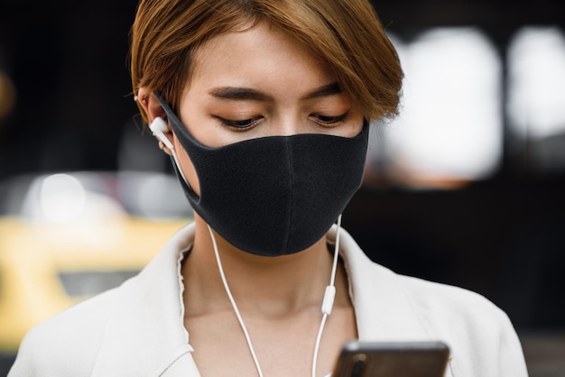 Young asian woman wearing face mask while using smartphone in the city of bangkok thailand