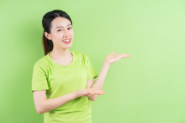 Young Asian woman wearing green shirt and posing on green background