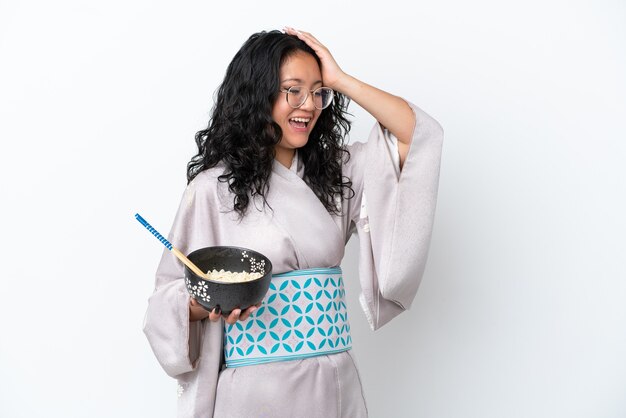 Young asian woman wearing kimono isolated on white background has realized something and intending the solution while holding a bowl of noodles with chopsticks