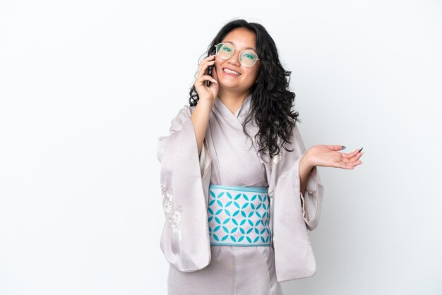 Young asian woman wearing kimono isolated on white background keeping a conversation with the mobile phone with someone