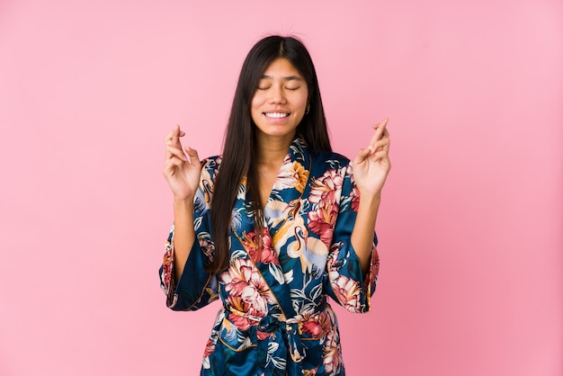 Young asian woman wearing a kimono pajamas crossing fingers for having luck