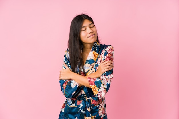 Young asian woman wearing a kimono pajamas hugs, smiling carefree and happy.