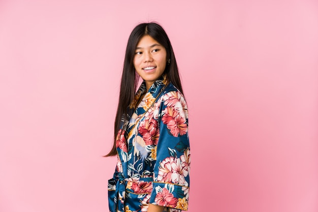Молодая азиатская женщина нося пижаму кимоно смотрит в сторону усмехаясь, жизнерадостная и приятная.