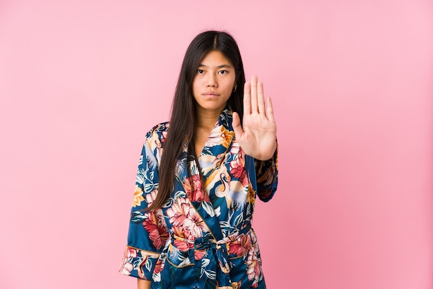 Young asian woman wearing a kimono pajamas standing with outstretched hand showing stop sign, preventing you.