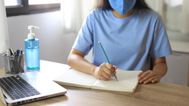 Young asian woman wearing medical facial handmade mask working alone distancing policy with hand sanitizer gel during coronavirus or covid19 virus outbreak a new normal concept