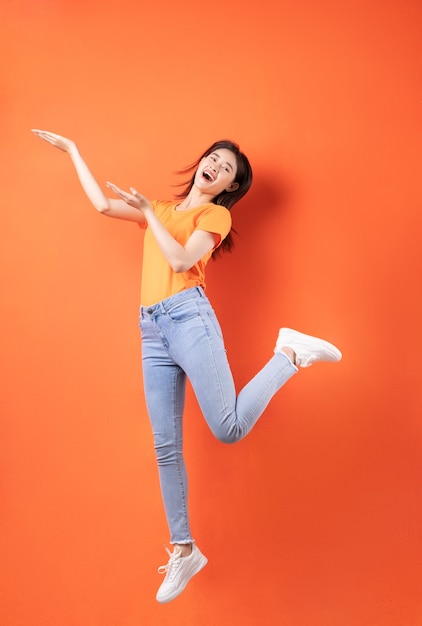 Young Asian woman wearing orange T-shirt jumping on orange