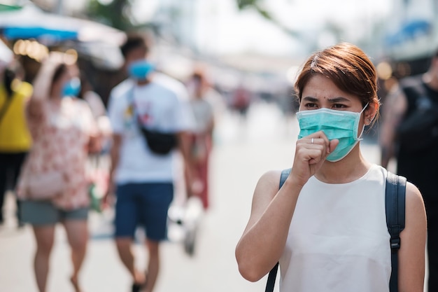 Giovane donna asiatica che indossa una maschera di protezione contro il romanzo coronavirus (2019-ncov) o wuhan coronavirus al mercato del fine settimana di chatuchak, punto di riferimento e popolare per le attrazioni turistiche