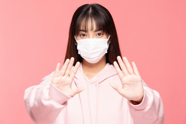 보호 벽 또는 분홍색 벽, 건강 관리 및 코로나 바이러스 개념에 보호 바이러스 및 대기 오염 만들기 손 중지 바이러스에 대한 보호 마스크 또는 수술 용 마스크를 착용하는 젊은 아시아 여자