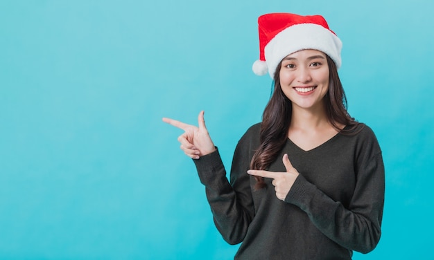 Giovane donna asiatica che indossa il cappello di babbo natale e indicando