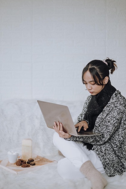 Young Asian woman wearing scarf and knitted sweater working on a laptop at home