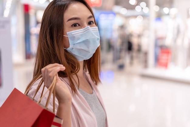 Young asian woman wearing surgical mask shopping in clothes store at mall