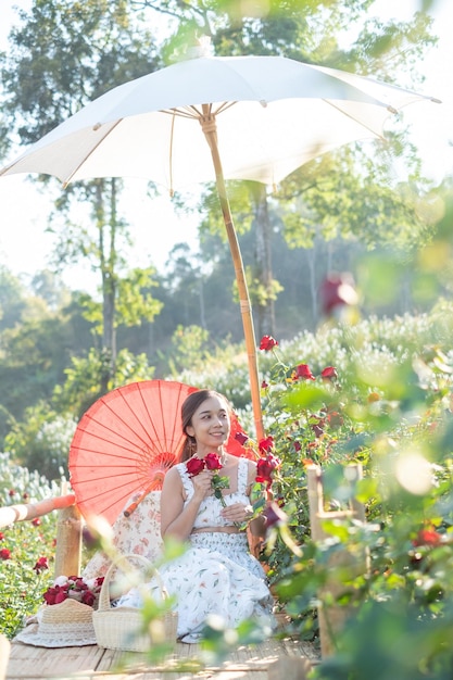 Foto giovane donna asiatica che indossa un abito bianco posa con una rosa nel roseto