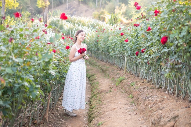 Young Asian woman wearing a white dress poses with a rose in rose garden