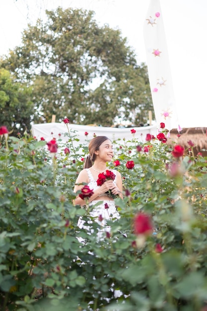 Foto giovane donna asiatica che indossa un abito bianco posa con una rosa nel roseto