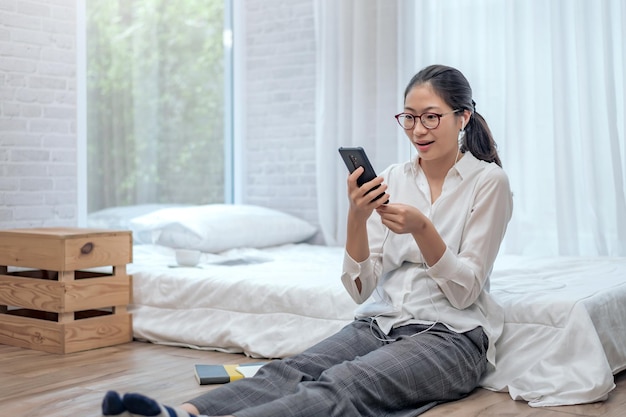 Foto la giovane donna asiatica indossa le cuffie per parlare e videoconferenza sul cellulare in camera da letto a casa