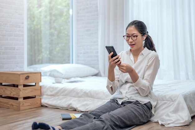 사진 젊은 아시아 여성은 헤드폰을 끼고 집에 있는 침실에서 휴대폰으로 대화하고 화상 회의를 합니다.