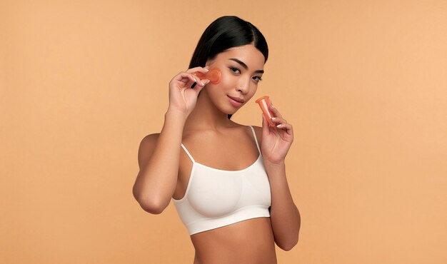 A young asian woman in white lingerie and clean radiant skin makes a vacuum massage of the face with silicone cans on beige