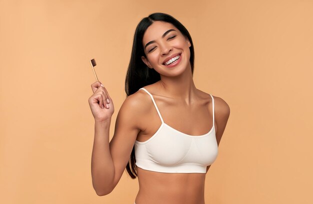 Young asian woman in white lingerie with a toothbrush and white teeth on beige. dental hygiene concept