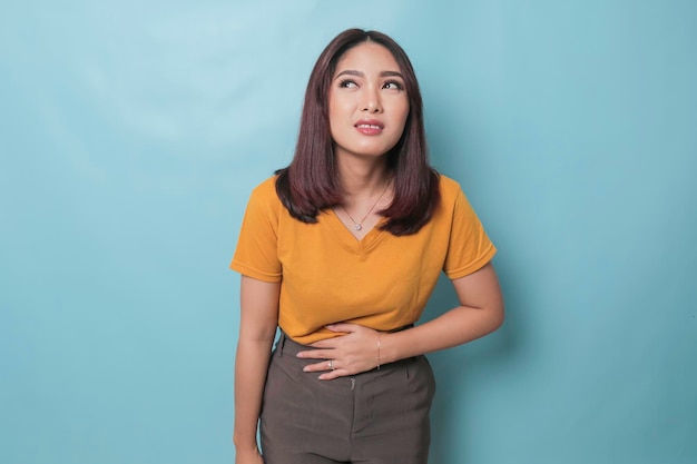 Young Asian woman with arms on stomach and bending over with stomachache expression