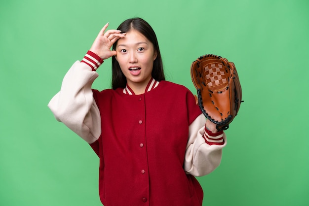 Young asian woman with baseball glove over isolated background doing surprise gesture while looking to the side