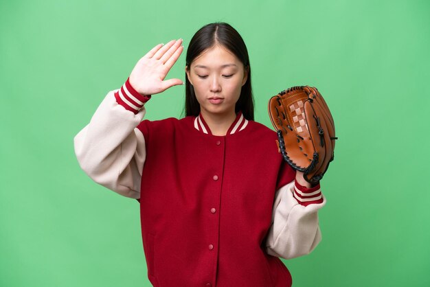 Young asian woman with baseball glove over isolated background making stop gesture and disappointed