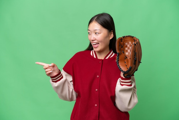 Young asian woman with baseball glove over isolated background pointing finger to the side and presenting a product