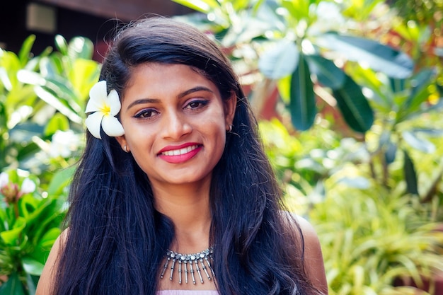 Young asian woman with black hair plumeria and fresh skin looking and smiling at the camera on park summer background