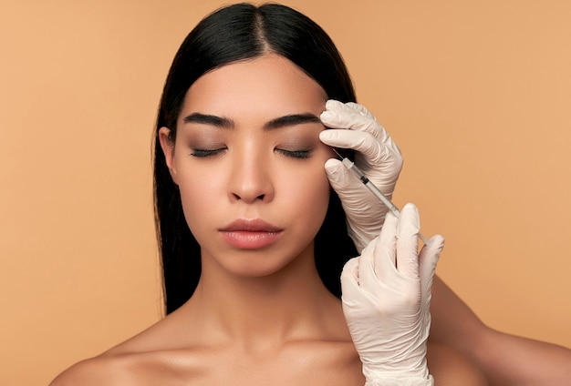 Una giovane donna asiatica con una pelle pulita e radiosa riceve iniezioni di botox per rassodare i contorni, aumentare le labbra sul beige